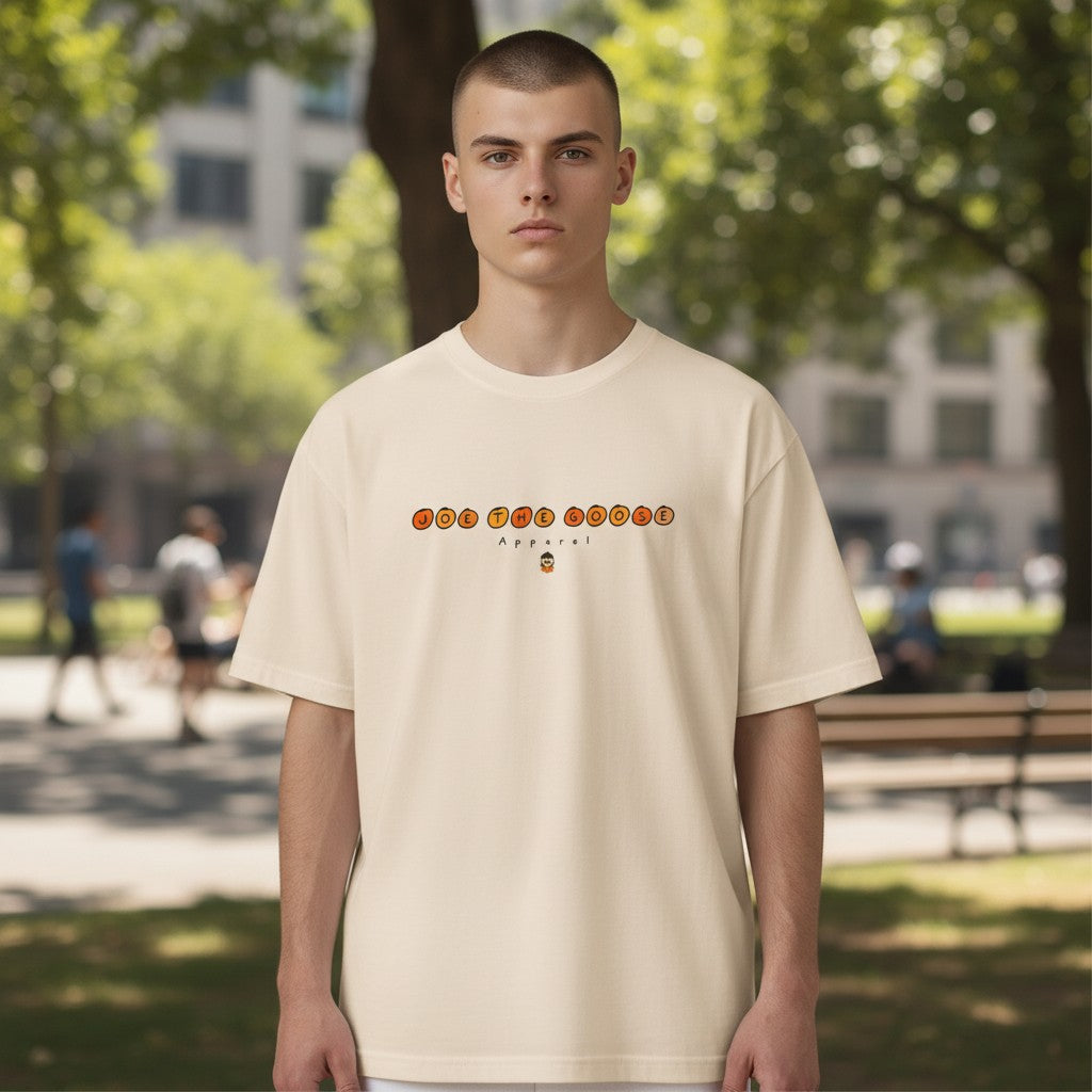 Man wearing a cream Joe the Goose Apparel heavy cotton classic tee with orange circle logo in a park setting.