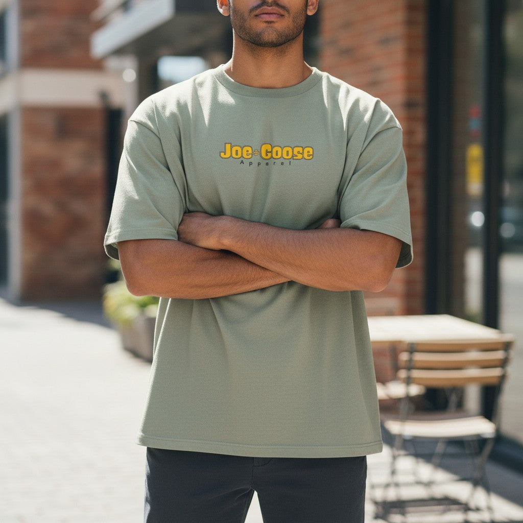 A man wearing a sage green Joe the Goose Apparel heavy weight cotton t-shirt with a relaxed fit and dropped shoulders.