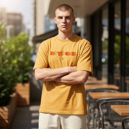 A man wearing a mustard yellow Joe the Goose Apparel heavy cotton t-shirt with a graphic logo, standing outdoors.