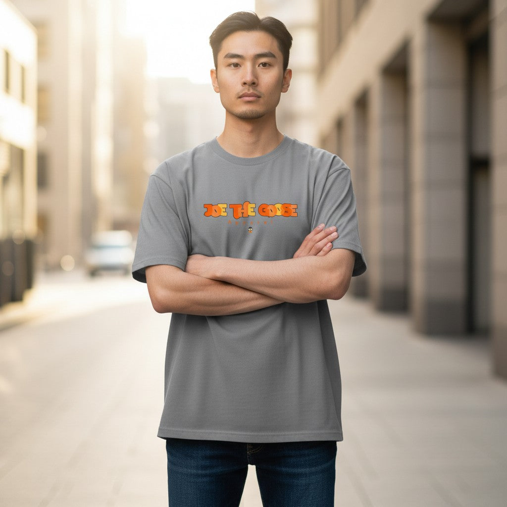 Man wearing a grey Joe the Goose Apparel heavy cotton t-shirt with a stained glass style logo, standing in a city.