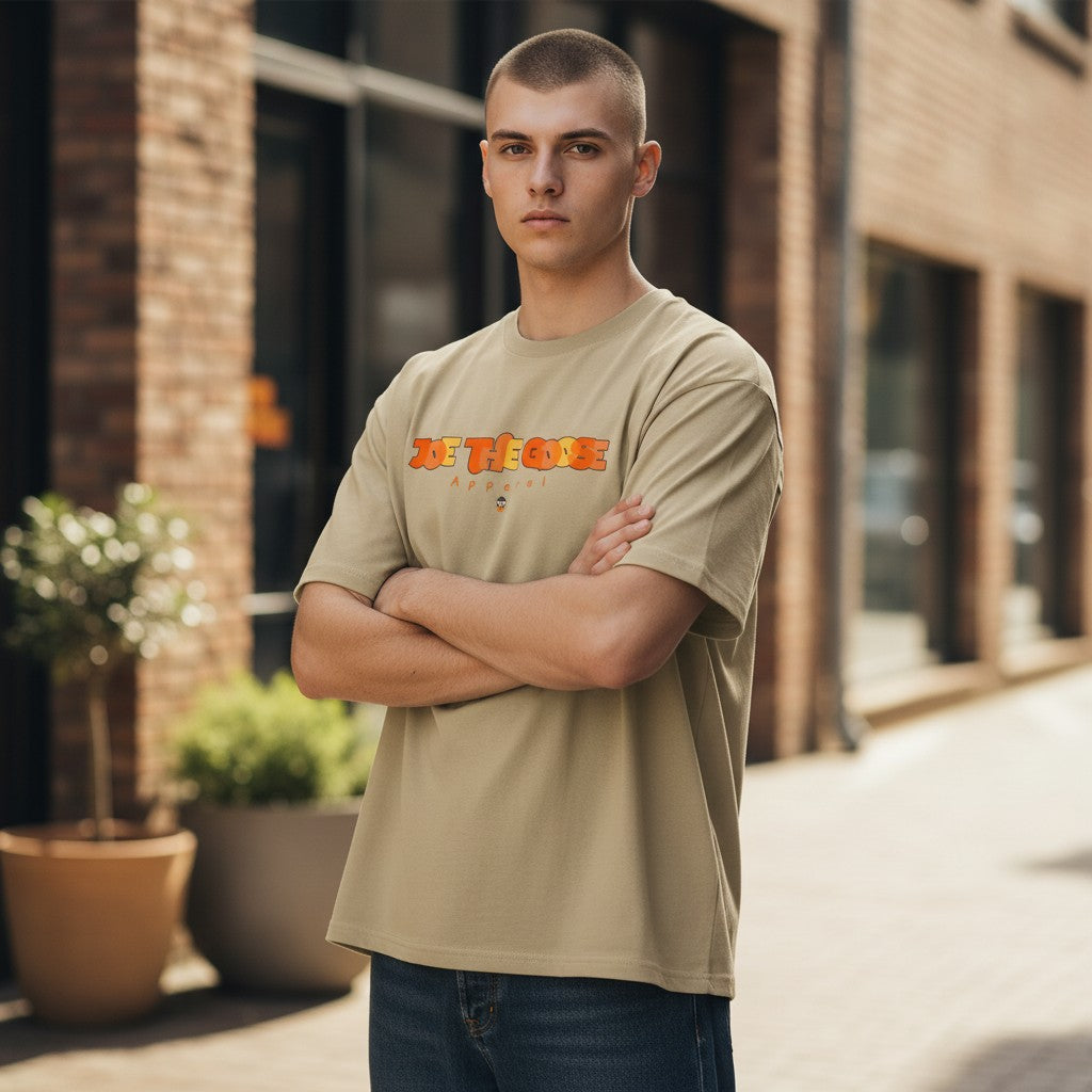 Man wearing a beige Joe the Goose Apparel Stained Glass Goose graphic t-shirt with arms crossed outdoors.