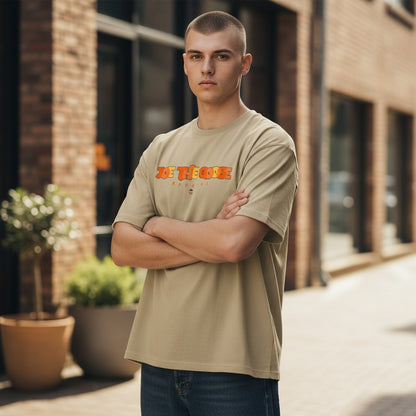 Man wearing a beige Joe the Goose Apparel Stained Glass Goose graphic t-shirt with arms crossed outdoors.